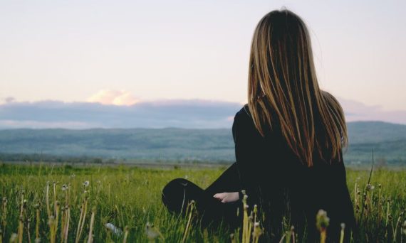 Woman enjoying peace in a lush green field with a scenic mountain view during sunset.